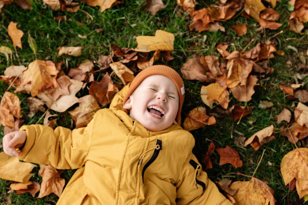 little boy lying on the ground in autumn leaves and laugh